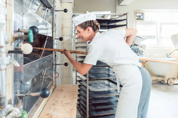Baker woman getting bread out of bakery oven — Stock Photo, Image