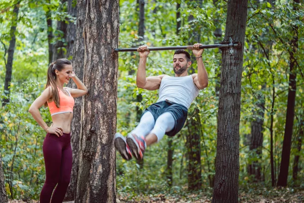 Woman watches man doing exercises on high bars