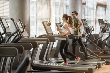 Genç adam ve koşu bandı üzerinde yan yana çalışırken gülümseyen kadın