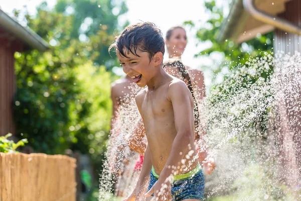 Boy cooling down with garden hose, family in the background — Stock Photo, Image