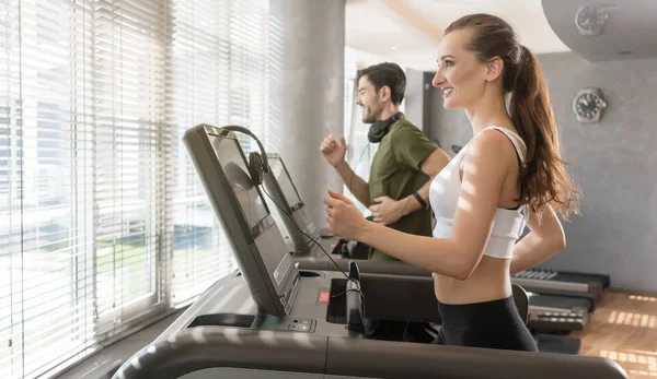 Young woman listening to music while running on a modern treadmill — Stock Photo, Image