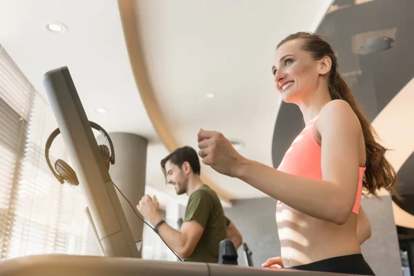 Mujer joven escuchando música mientras corre en una cinta de correr moderna — Foto de Stock