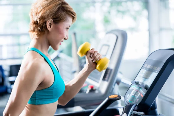 Asian woman walking on treadmill holding dumbbell — Stock Photo, Image