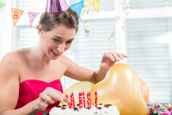 Retrato de una hermosa mujer sonriendo mientras pone velas rojas en un pastel —  Fotos de Stock