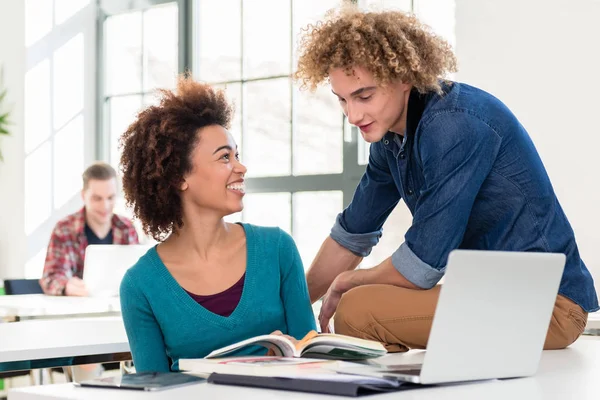 Two friendly classmates of different nationalities talking about a textbook — Stock Photo, Image