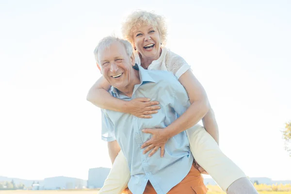 Gelukkig senior man lachen terwijl de uitvoering van zijn partner op zijn rug — Stockfoto