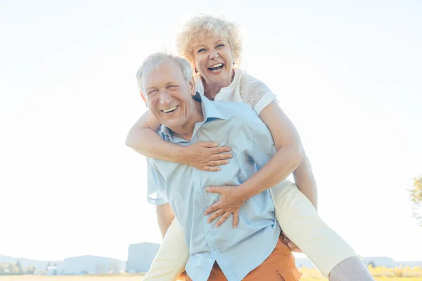 Glücklicher Senior lacht, während er seine Partnerin auf dem Rücken trägt — Stockfoto