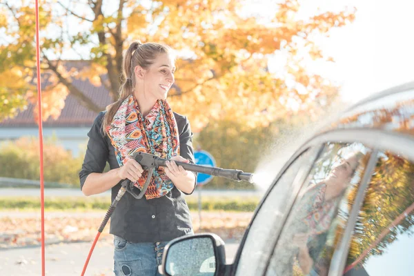 Mujer usando boquilla de alta presión para limpiar su coche — Foto de Stock