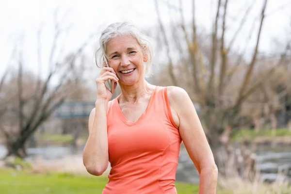 Senior vrouw in de sport kleding ontvangen oproep op haar mobiele telefoon — Stockfoto