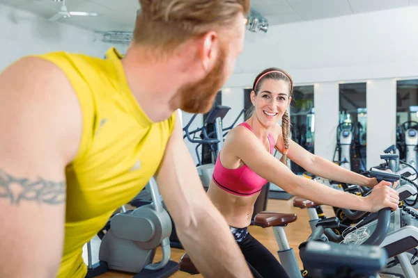 Kvinnan ler på den stiliga mannen bredvid henne medan Cykling på gymmet — Stockfoto