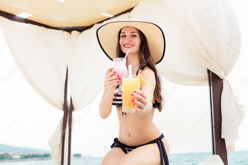 Woman in swimwear offering a cocktail on the beach as refreshment