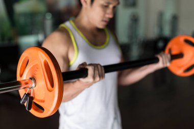 Determined young man holding a barbell while exercising bicep curls clipart