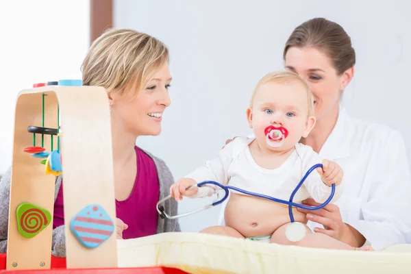 Leuke en gezonde babymeisje speelt met de stethoscoop tijdens onderzoek — Stockfoto