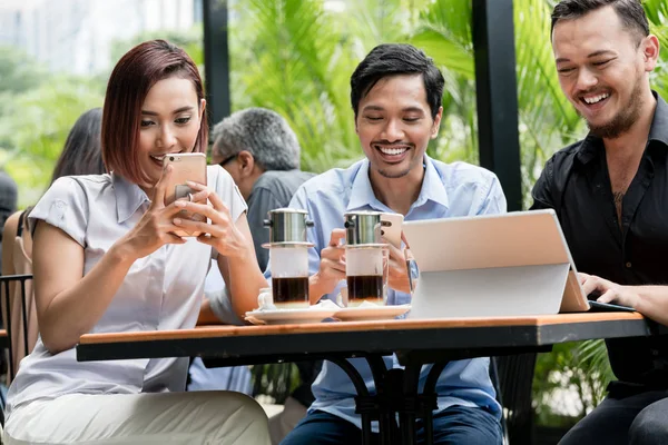 Vrienden met behulp van apparaten die zijn aangesloten op het draadloze internet van een moderne coffeeshop — Stockfoto