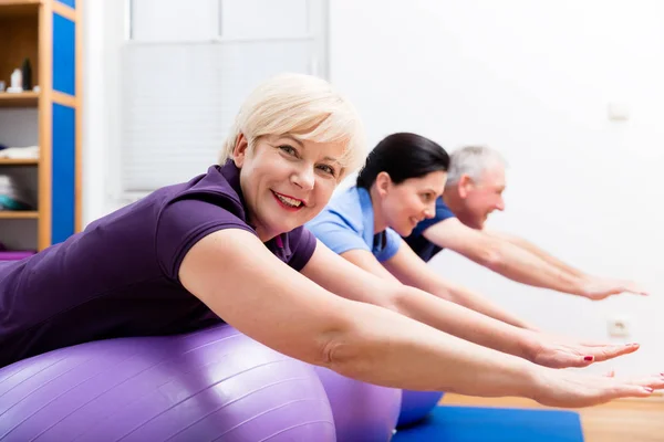 Physio zeigt Senioren, wie man Gymnastikball für Übungen einsetzt — Stockfoto