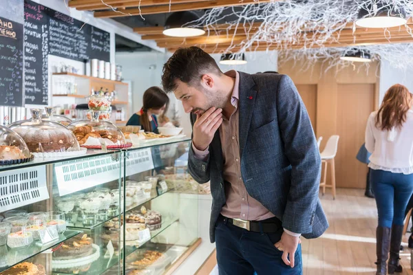 Besluiteloos man kijken naar verschillende taarten blootgesteld in de showcase — Stockfoto