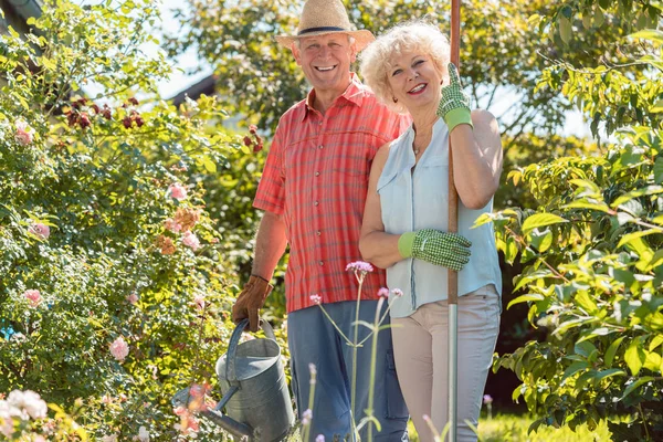 Активная счастливая пожилая женщина, стоящая рядом с мужем во время работы в саду — стоковое фото