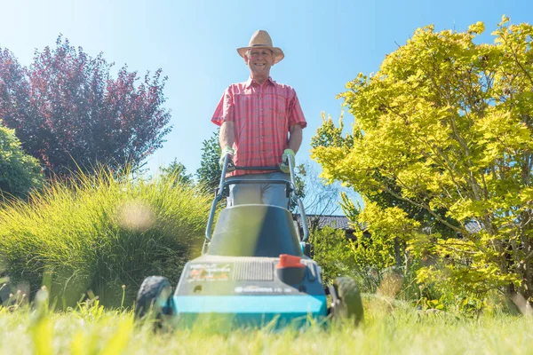 Homem sênior ativo sorrindo ao usar uma máquina de corte de grama — Fotografia de Stock