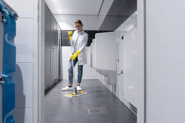 Limpeza senhora esfregando o chão no banheiro dos homens — Fotografia de Stock