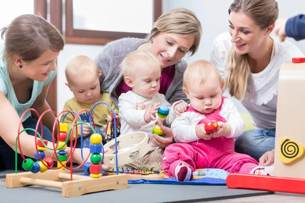 Three happy mothers watching their babies playing with safe toys — Stock Photo, Image