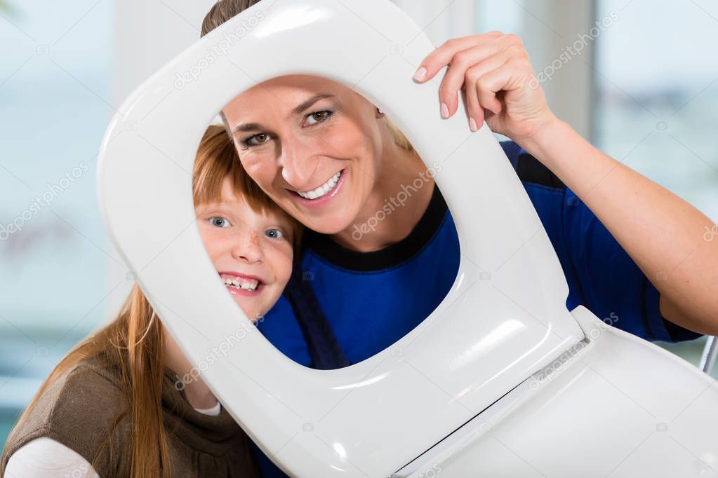 Portrait of a woman and her daughter looking at camera through a toilet seat