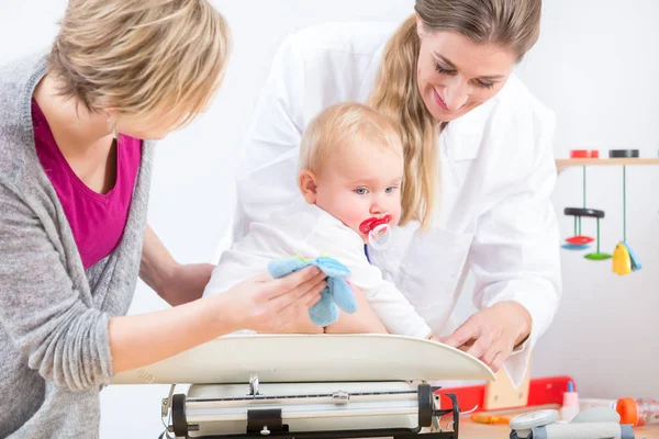 Bir kız bebek ağırlık ölçme sırasında gülümseyen Pediatrik bakım uzmanı — Stok fotoğraf