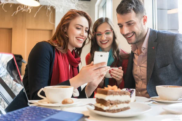 Tři mladí přátelé pomocí mobilního telefonu pro zábavu během přestávky na kávu — Stock fotografie