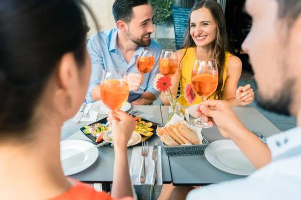 Dois jovens casais felizes brindam enquanto se sentam juntos no restaurante — Fotografia de Stock