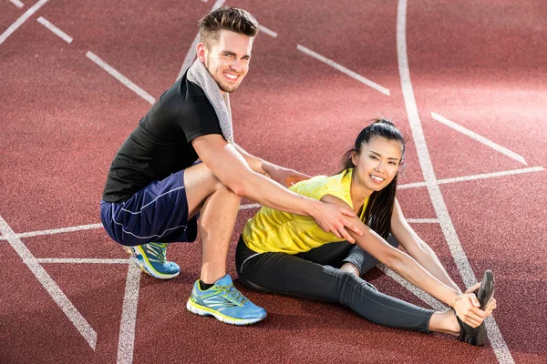 Man and woman on cinder track of sports arena stretching exercises