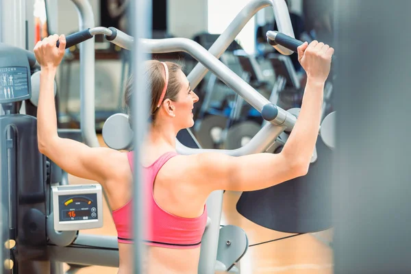 Bakifrån av en vältränad kvinna med tonade armar och rygg träning på gymmet — Stockfoto