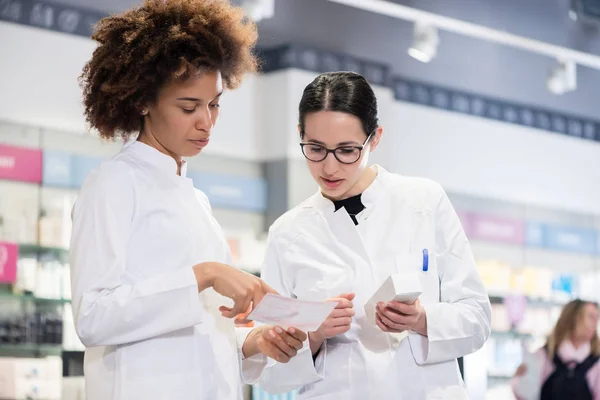 Dos farmacéuticos que comparan medicamentos con respecto a indicaciones y efectos secundarios —  Fotos de Stock