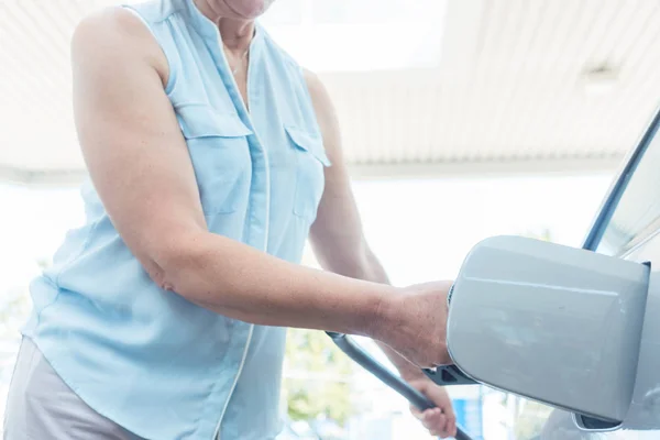 Активная пожилая женщина улыбается, заправляя бензобак своей машины — стоковое фото