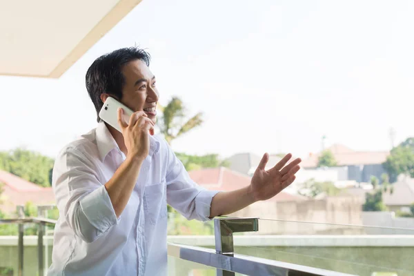 Azjatycki człowiek telefonicznie na balkonie z telefonu komórkowego — Zdjęcie stockowe