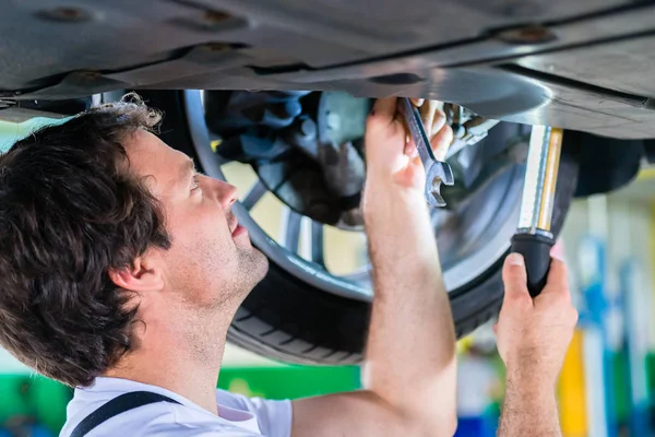 Mechanic working in car workshop on wheel — Stock Photo, Image
