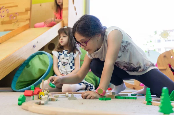 Girl playing with a wooden train circuit in the kindergarten — Stock Photo, Image