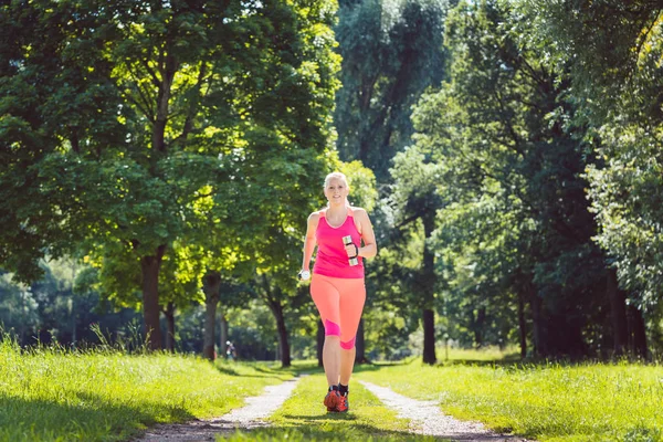 Woman running down a path on meadow with weight dumbbells — Stock Photo, Image