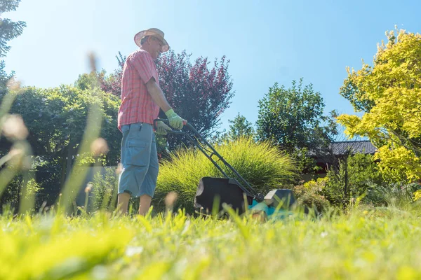 Homme âgé actif souriant tout en utilisant une machine à couper l'herbe — Photo