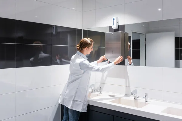 Femme de ménage recharge serviettes en papier dans les toilettes publiques — Photo