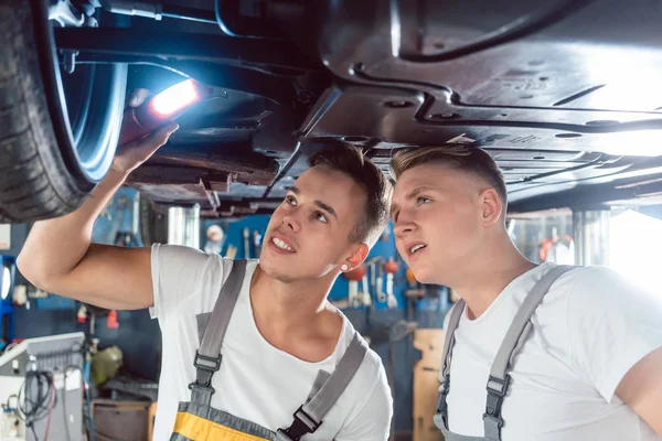 Dwóch mechaników samochodowych, analizując felgi uniesiony samochód — Zdjęcie stockowe