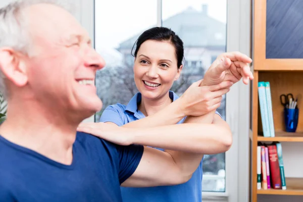 Oudere patiënt schouder training onder hulp van de therapeut — Stockfoto