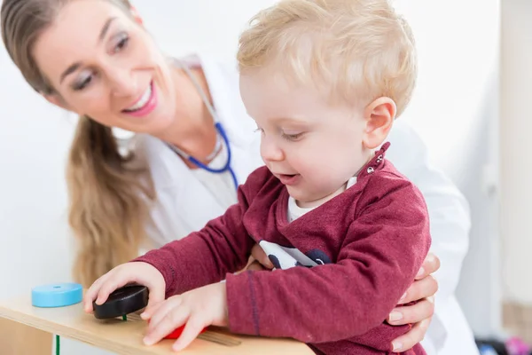 Cute active baby boy playing with toys during physical examination — Stock Photo, Image