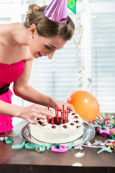 Porträtt av en vacker kvinna som ler samtidigt sätta röda ljus på en tårta — Stockfoto