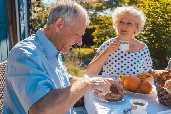 Mujer mayor y hombre desayunando sentados en su jardín — Foto de Stock