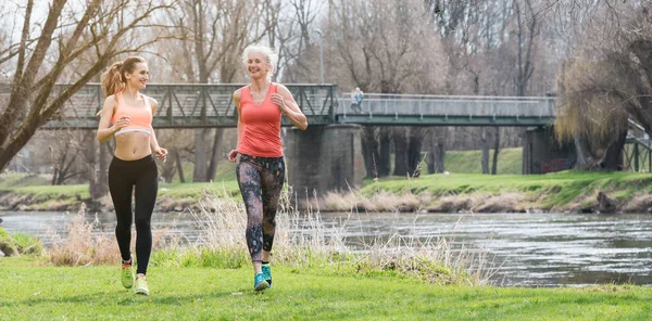 Mujer mayor y joven corriendo como deporte en un prado en primavera — Foto de Stock