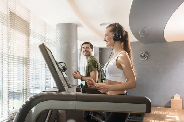 Young woman listening to music while running on a modern treadmill — Stock Photo, Image