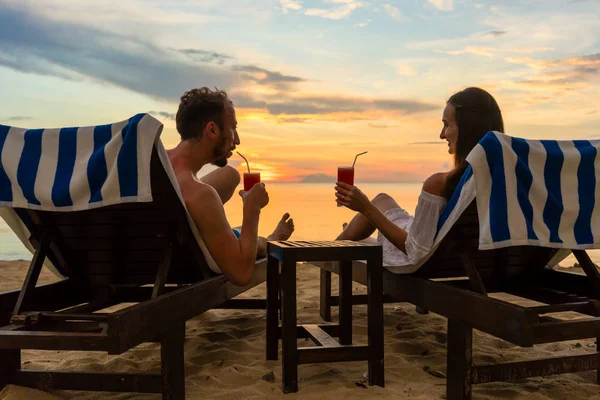 Młoda para picia koktajli na plaży o zachodzie słońca podczas wakacji — Zdjęcie stockowe
