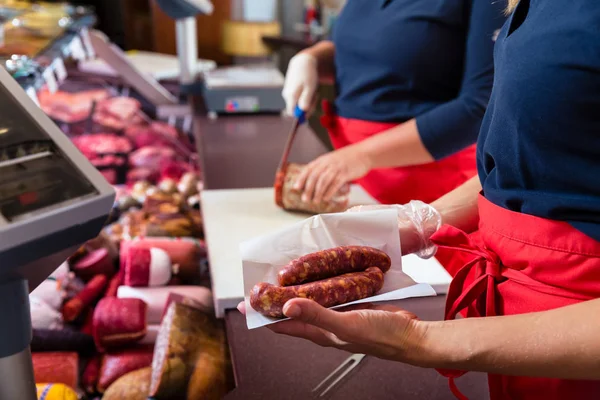 Женщины в мясном магазине продают мясо и колбасу — стоковое фото