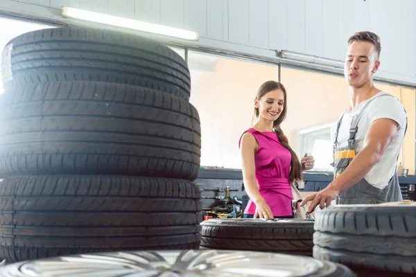 Mecánico auto guapo ayudando a un cliente a elegir entre varios neumáticos — Foto de Stock