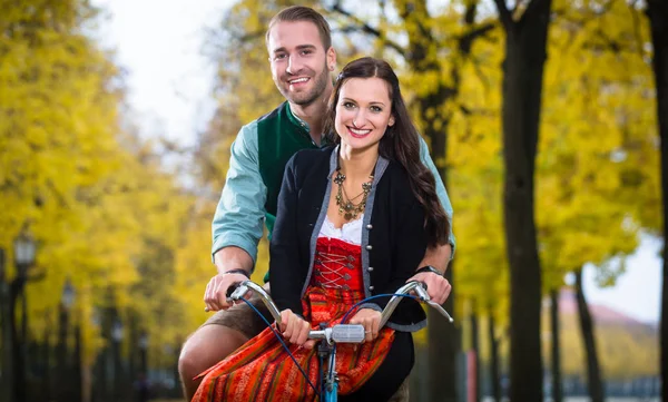 Couple en Dirndl et pantalon en cuir ensemble sur un vélo — Photo