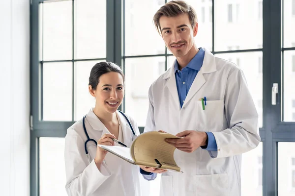 Dwóch lekarzy dedykowany uśmiechający się trzymając folder z dokumentacji medycznej — Zdjęcie stockowe